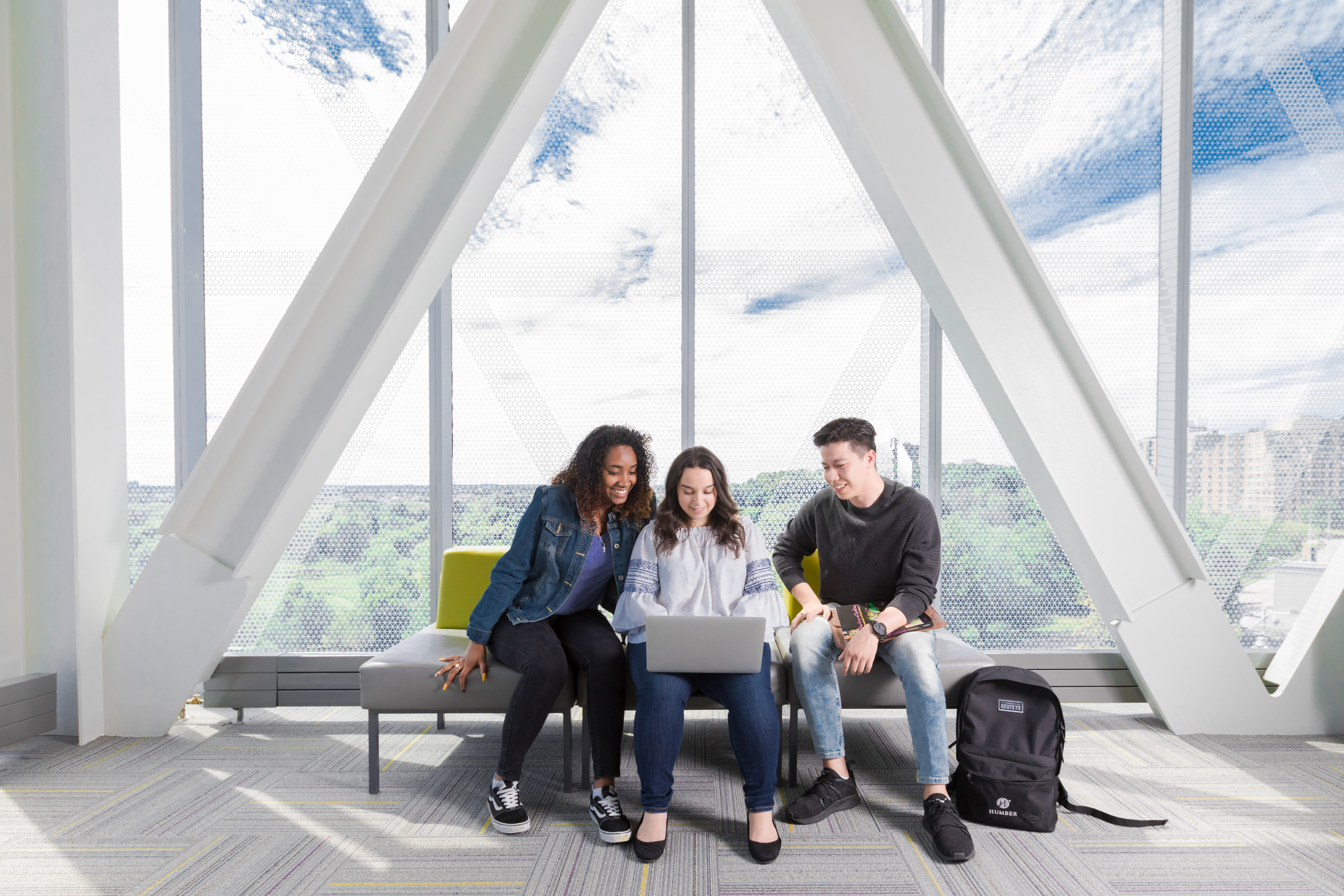 Three diverse students looking at a laptop together in front of a large window